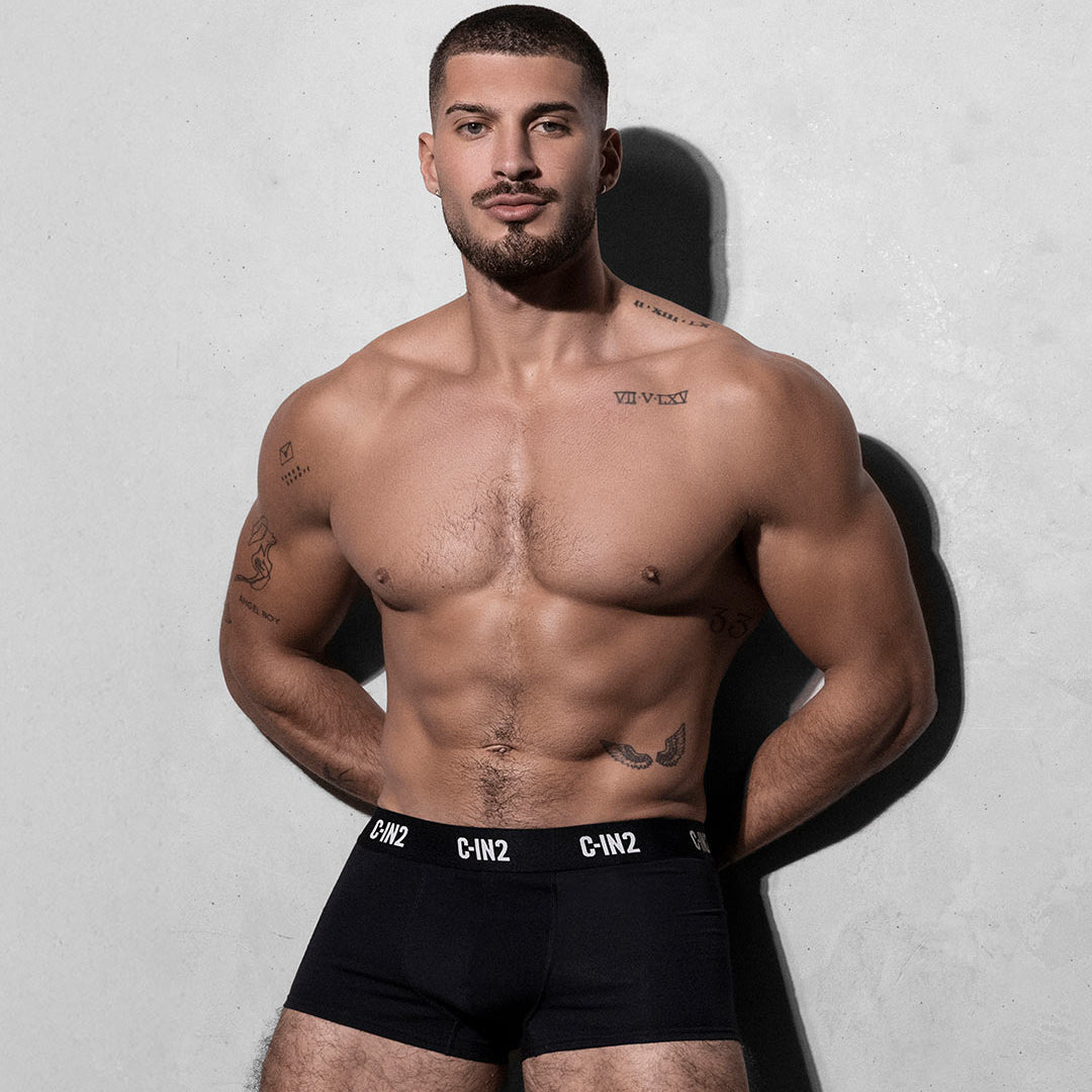 Man wearing black underwear with visible branding against a plain background