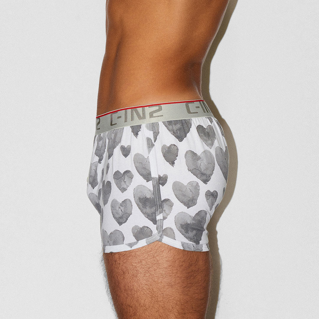 A side view of a male model wearing white boxer briefs with a gray heart pattern and a gray waistband featuring the brand name 'C-IN2'.