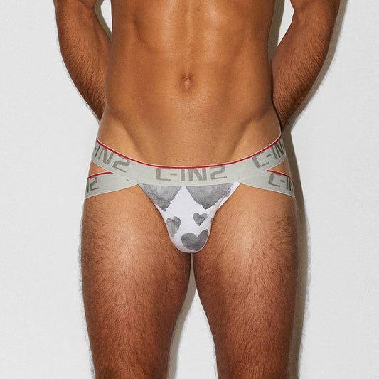 A close-up of a male model's lower torso wearing C-IN2 branded jockstrap. The underwear features a gray and white heart graphic on the front pouch and a light gray waistband with repeating C-IN2 branding.