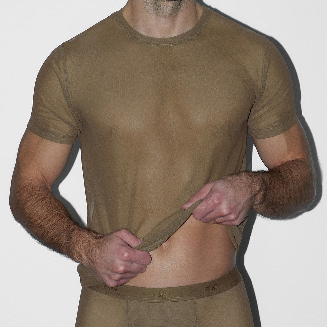 Man wearing a sheer beige t-shirt against a white background