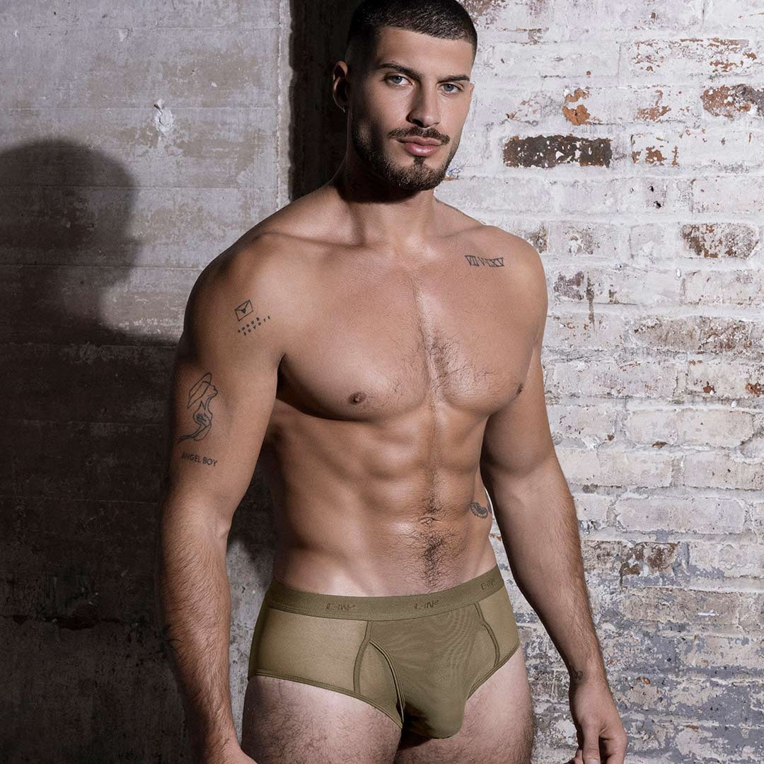 Man wearing a green underwear against a brick wall