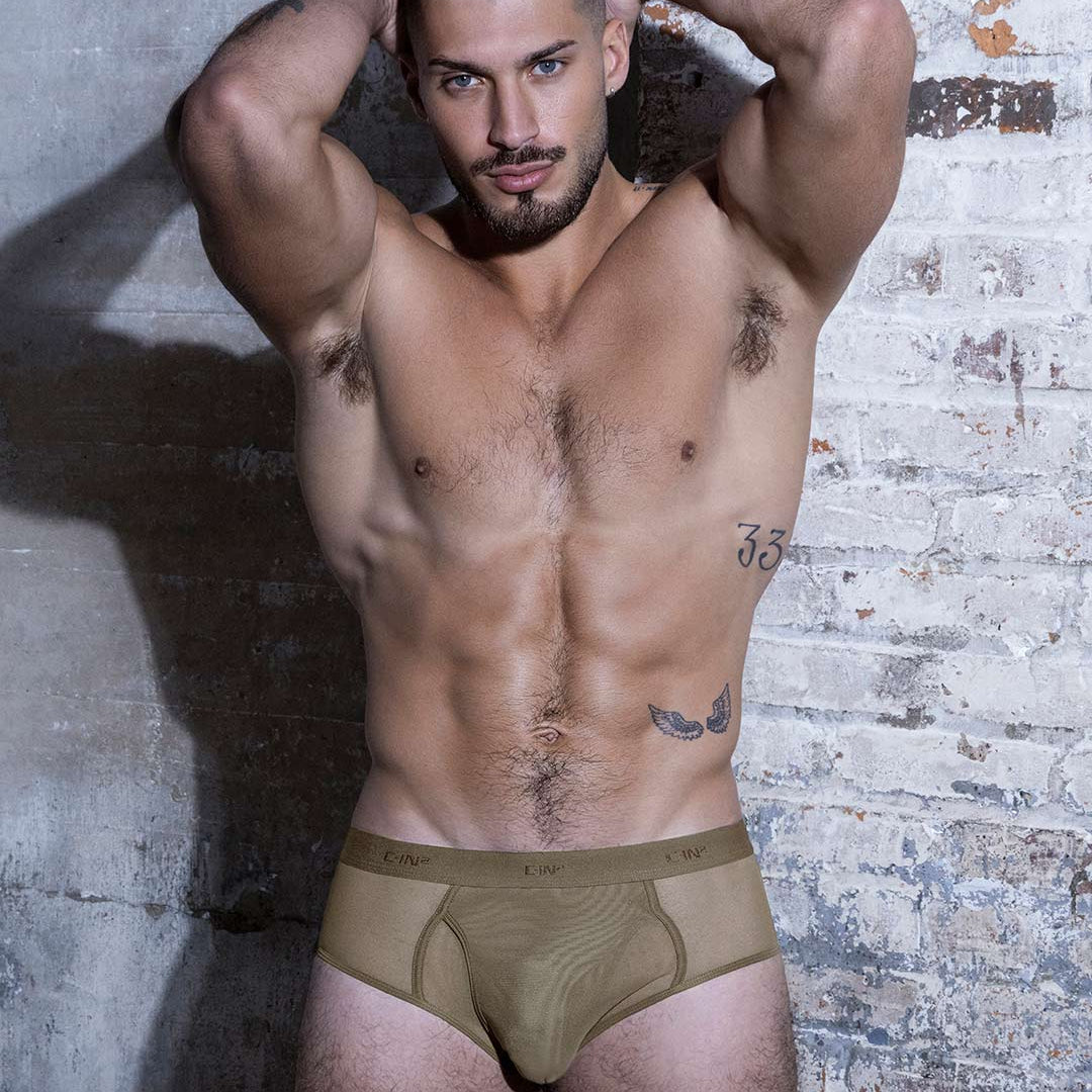 Man wearing beige underwear against a textured wall.