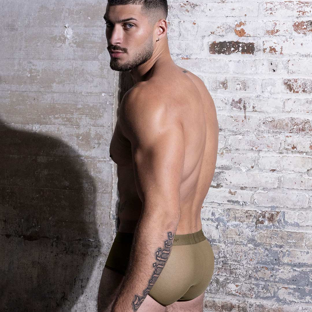 Man wearing beige underwear against a textured brick wall.