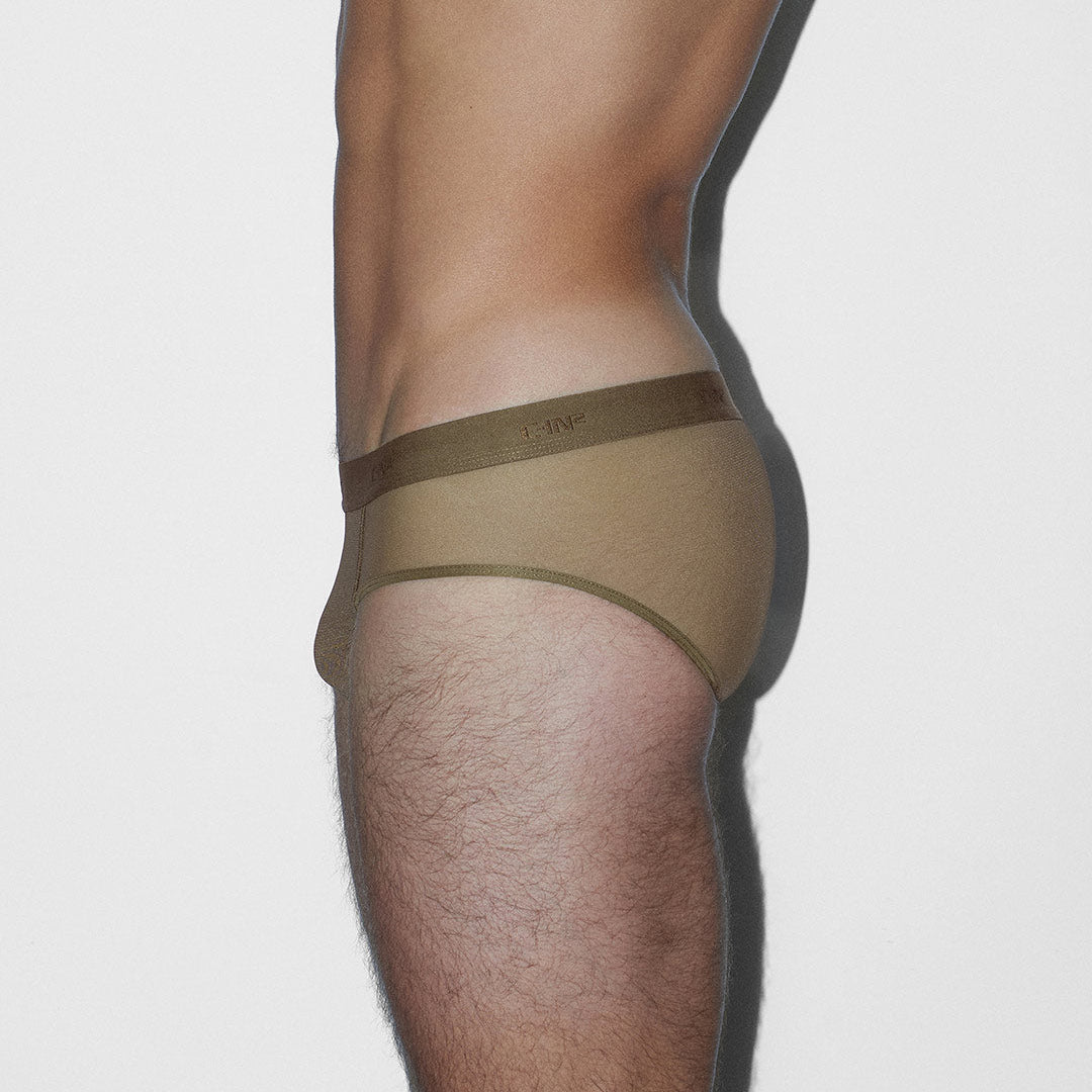 Side view of a model wearing beige briefs with a darker olive-brown waistband, shown against a plain light gray background.