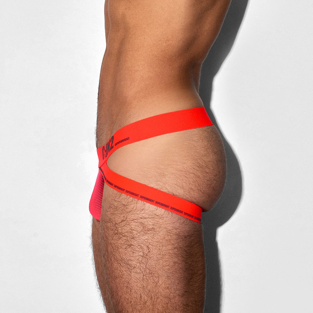 A close-up side view of a person's lower torso and upper thigh wearing bright neon orange-red jock with black printed text on a light gray background.