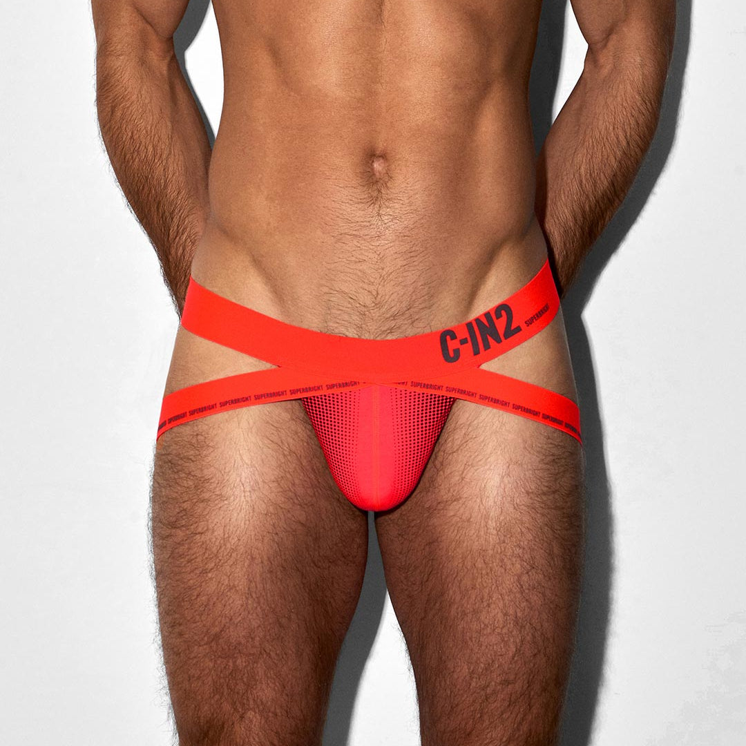 A close-up of a male model's lower torso wearing bright red jockstrap with wide red straps and black 'C-IN2' branding on the side, against a plain light background.