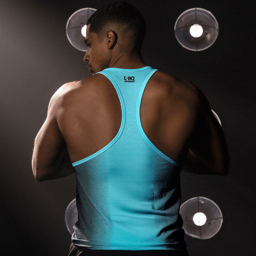 Man wearing a blue tank top with a C-IN2 logo on the back, standing against a dark background.