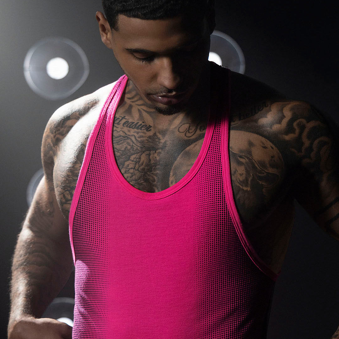 Man wearing a pink tank top with tattoos on a dark background