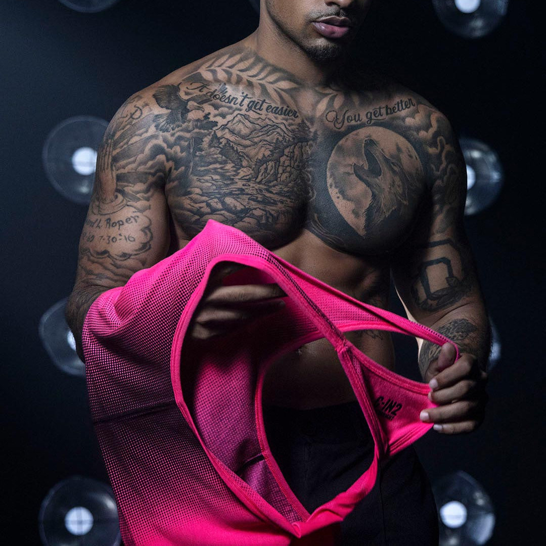 Man with tattoos holding a pink garment against a dark background