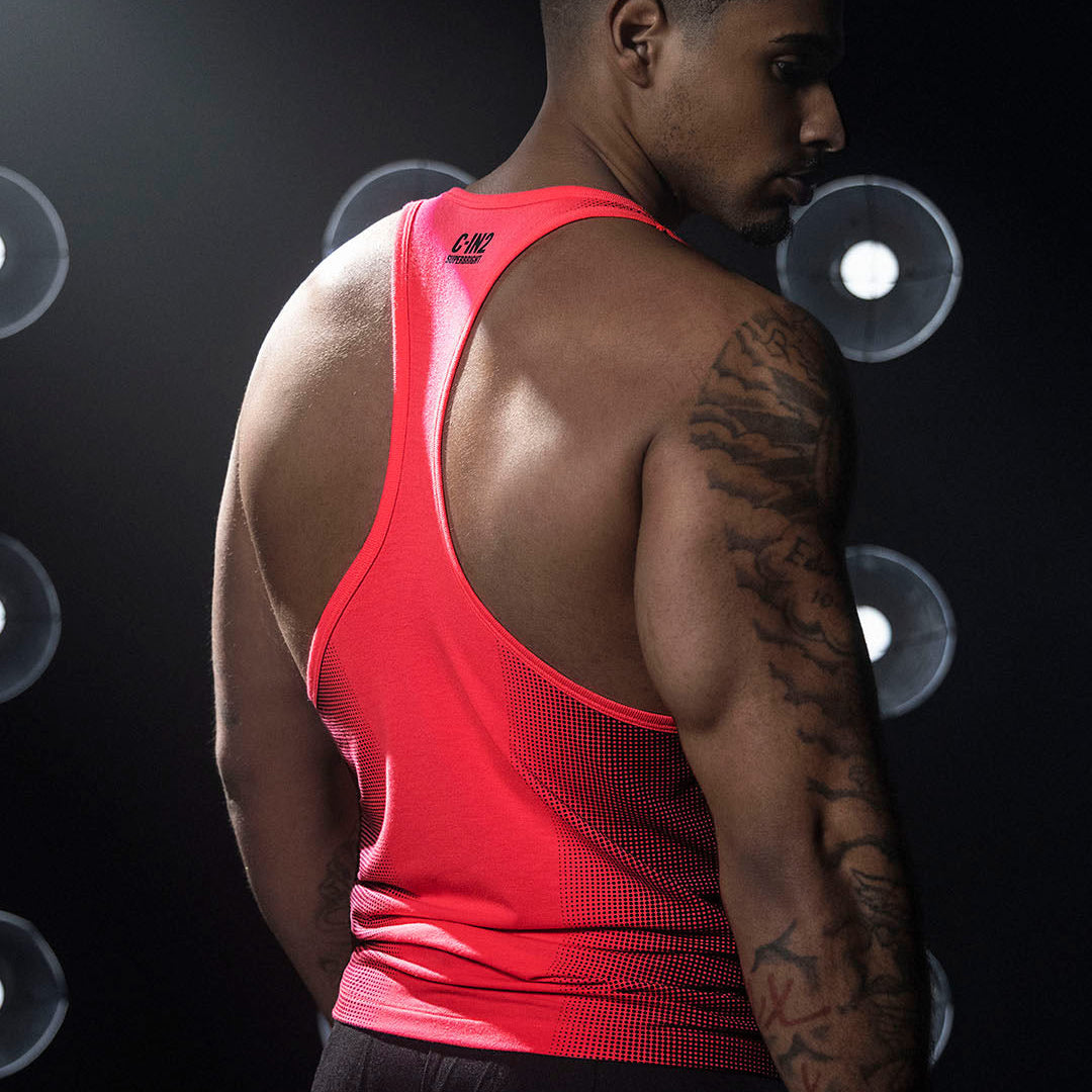 Man wearing a red tank top with a brand logo, standing against a dark background with light circular patterns.