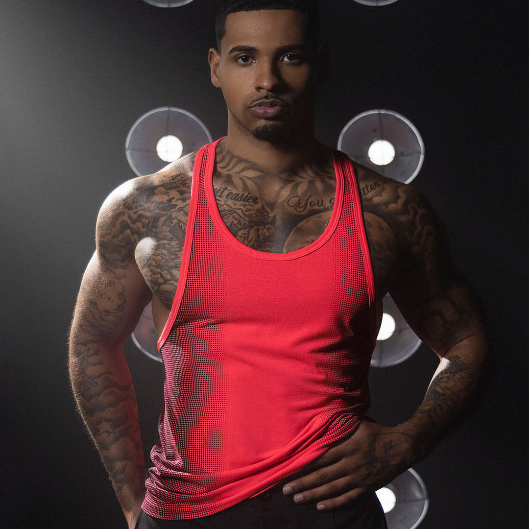 Man wearing a red tank top with tattoos on a dark background