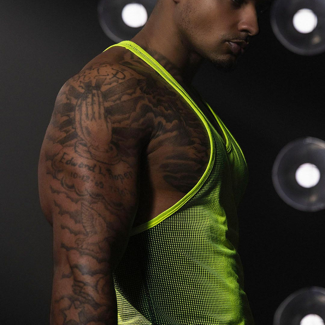 Man wearing a green tank top with tattoos on his arm against a dark background with light spots.