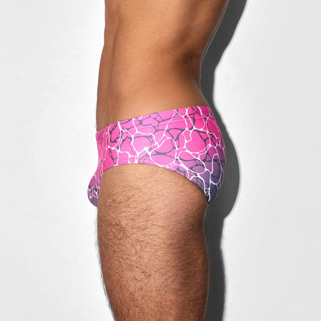 Pink and purple patterned swim brief on a person's leg against a white background