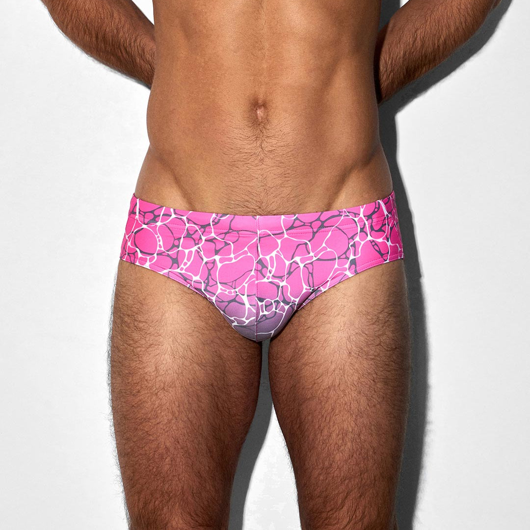 Man wearing pink bikini swim briefs with a geometric pattern on a white background