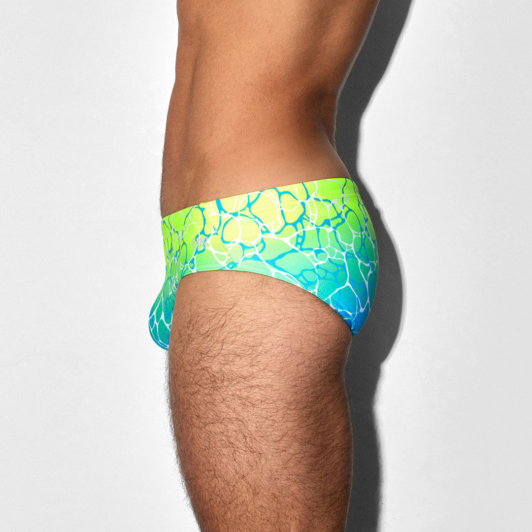 Green and blue patterned swim brief on a person against a white background