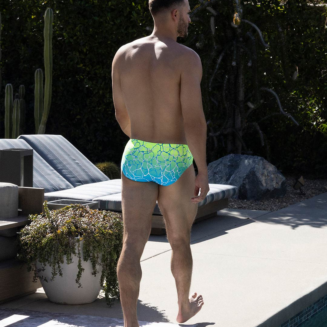 Man wearing colorful swim briefs standing outdoors near a pool