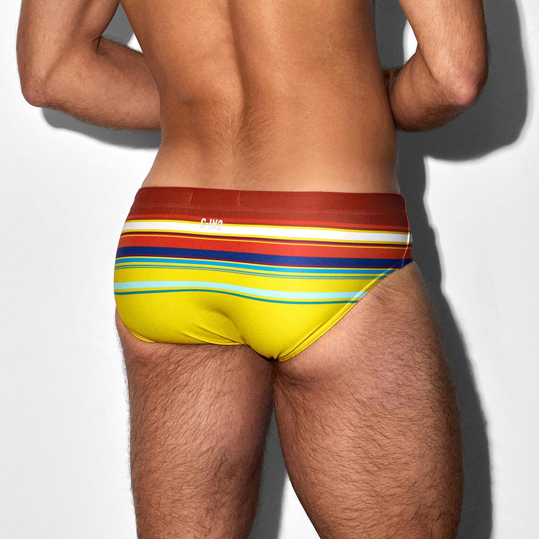 Man wearing colorful striped swim briefs with C-IN2 logo against a white background