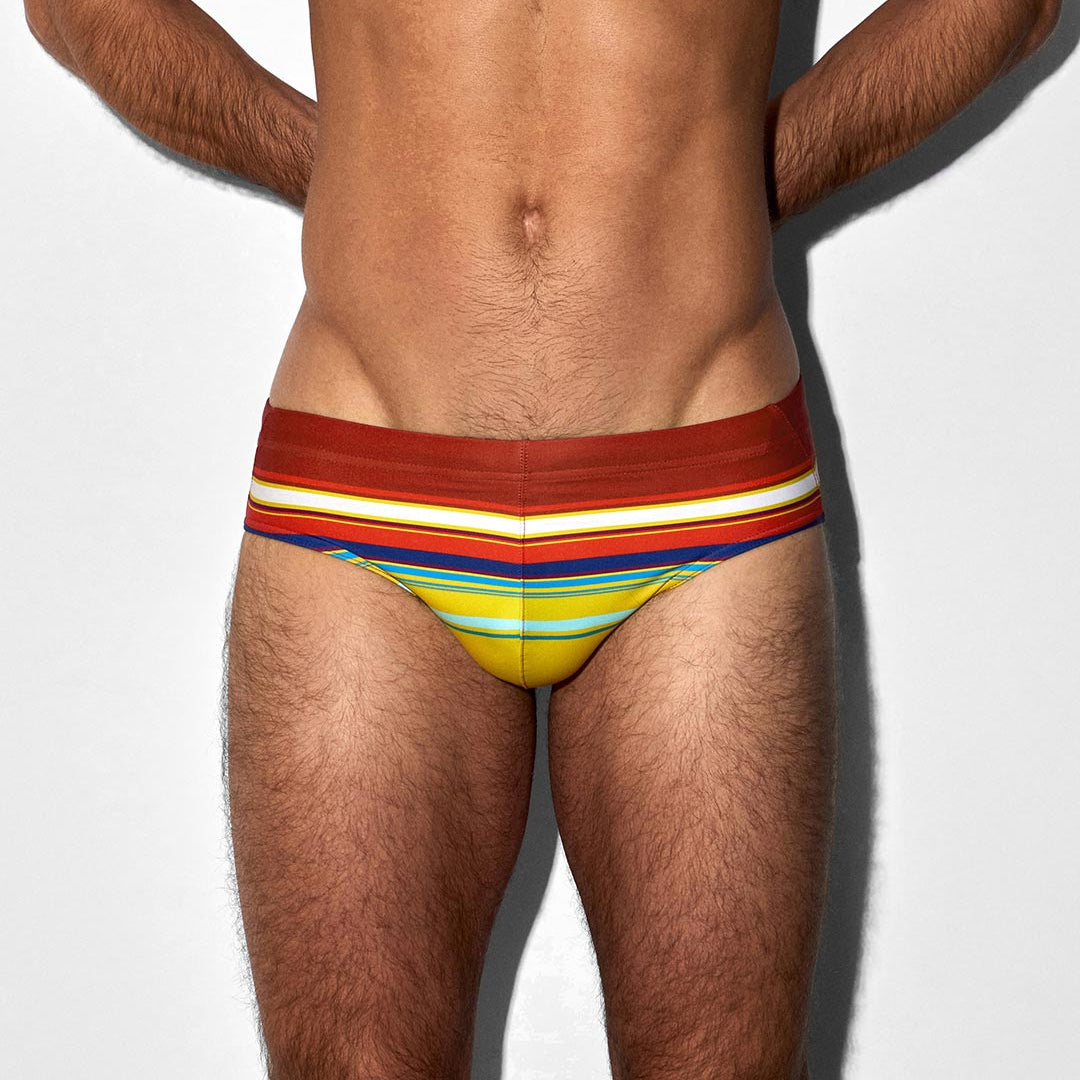 Man wearing colorful striped bikini swim briefs on a plain background