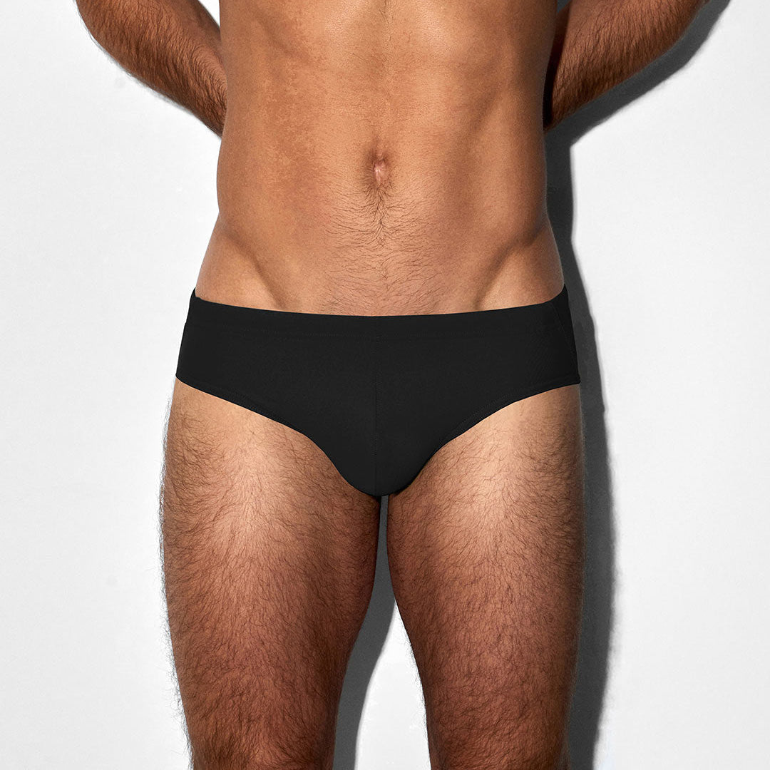 Man wearing black men's swim briefs against a white background