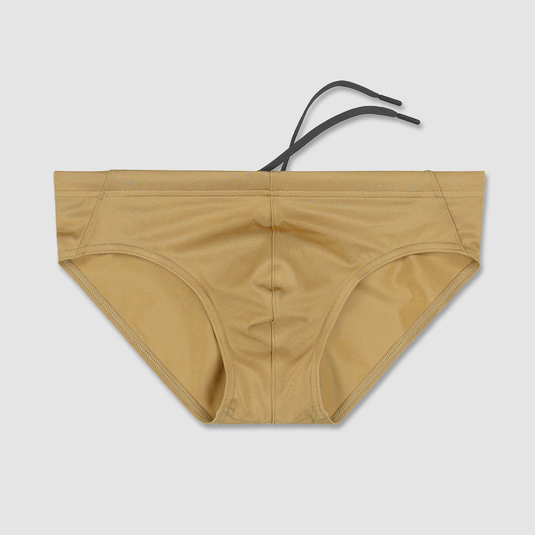 Champaign-nude colored bikini swim briefs with a black strap on a light gray background