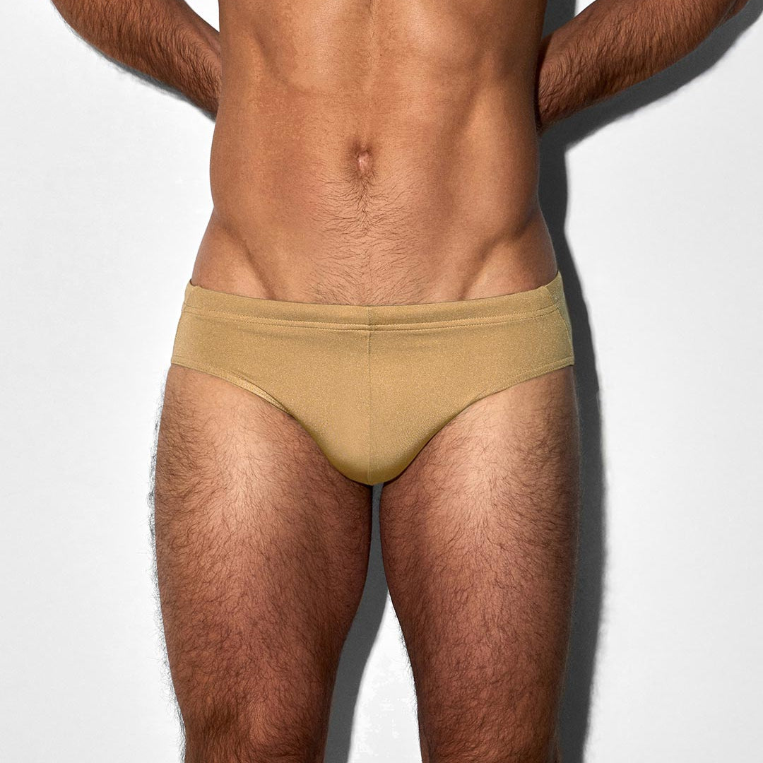 Man wearing champaign-nude colored swim brief against a white background
