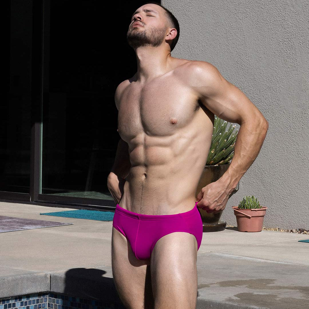 Man in pink swim trunks standing by a poolside.