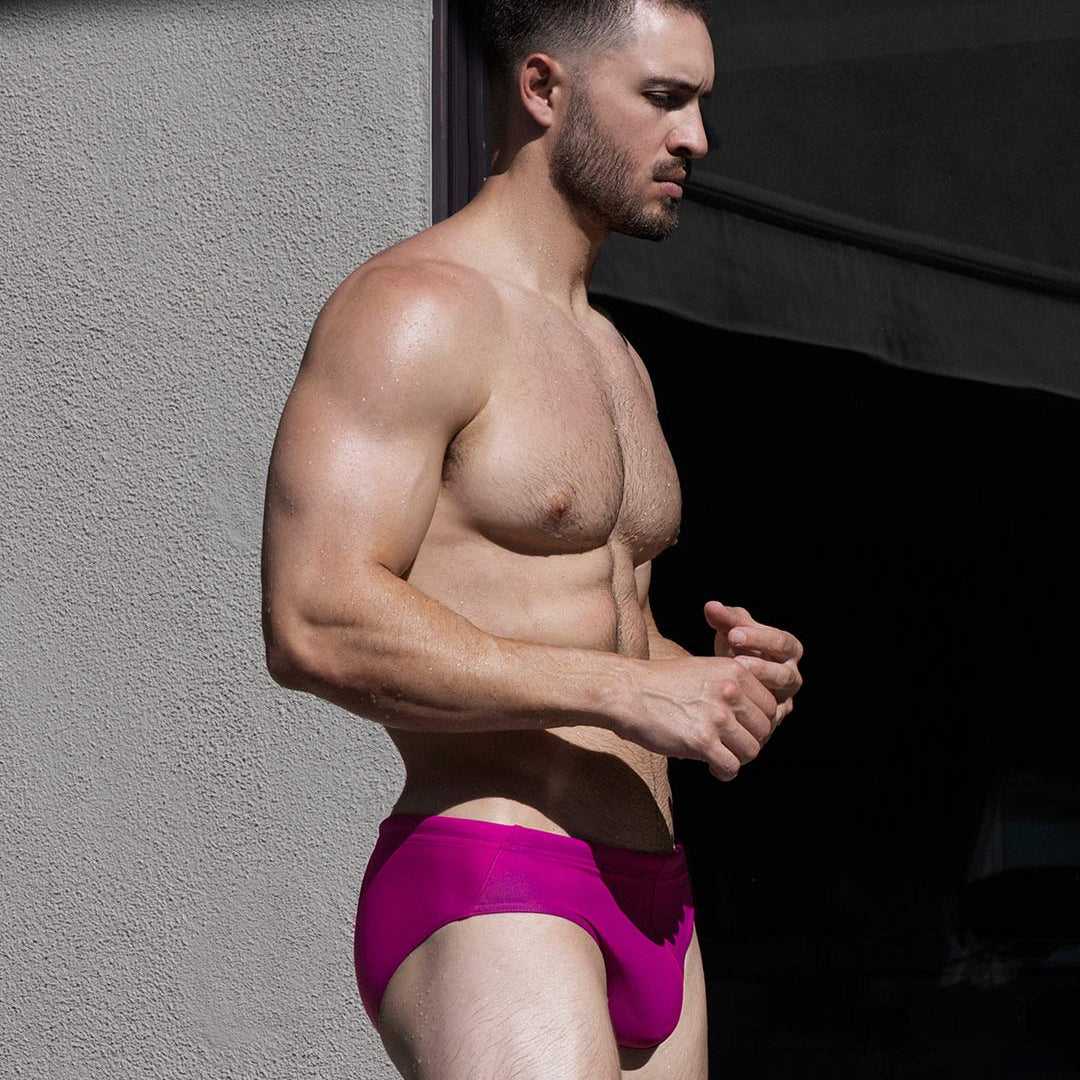 Man wearing bright pink swim briefs against a dark background