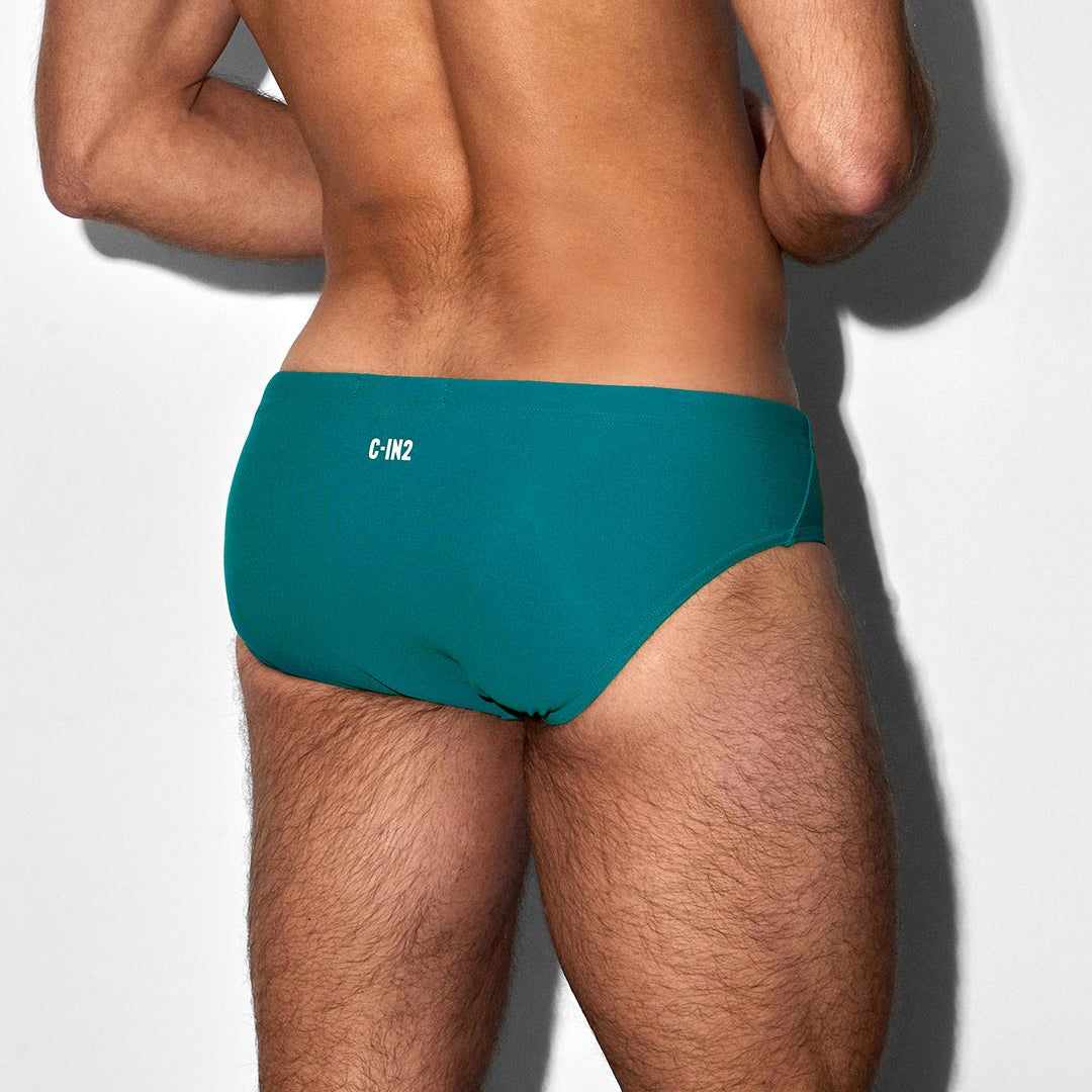 Teal swim brief with 'C-IN2' branding worn by a person on a white background