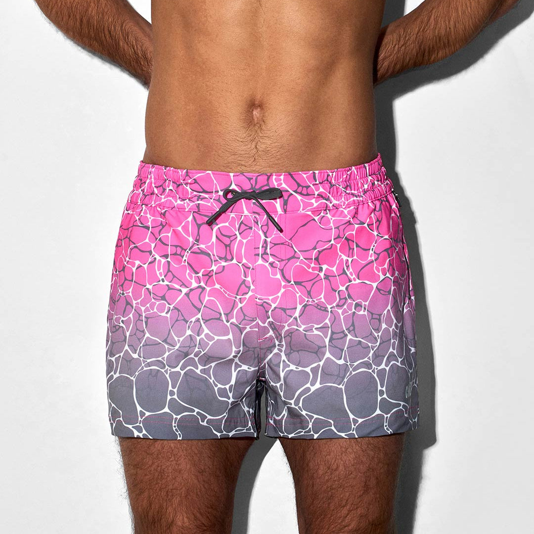 Person wearing pink and gray patterned swim shorts on a white background
