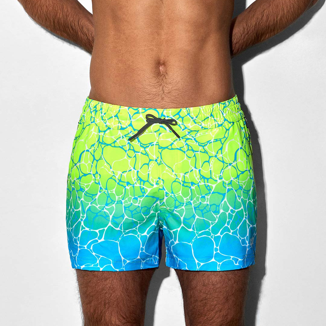 Man wearing bright green and blue patterned swim shorts on a white background