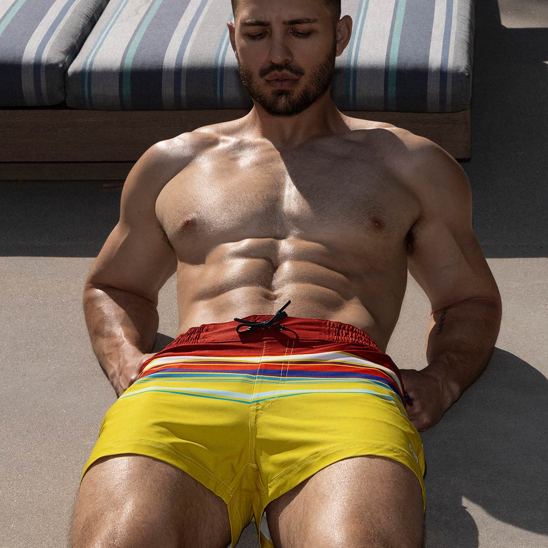 Man wearing colorful swim shorts sitting on a lounge chair.
