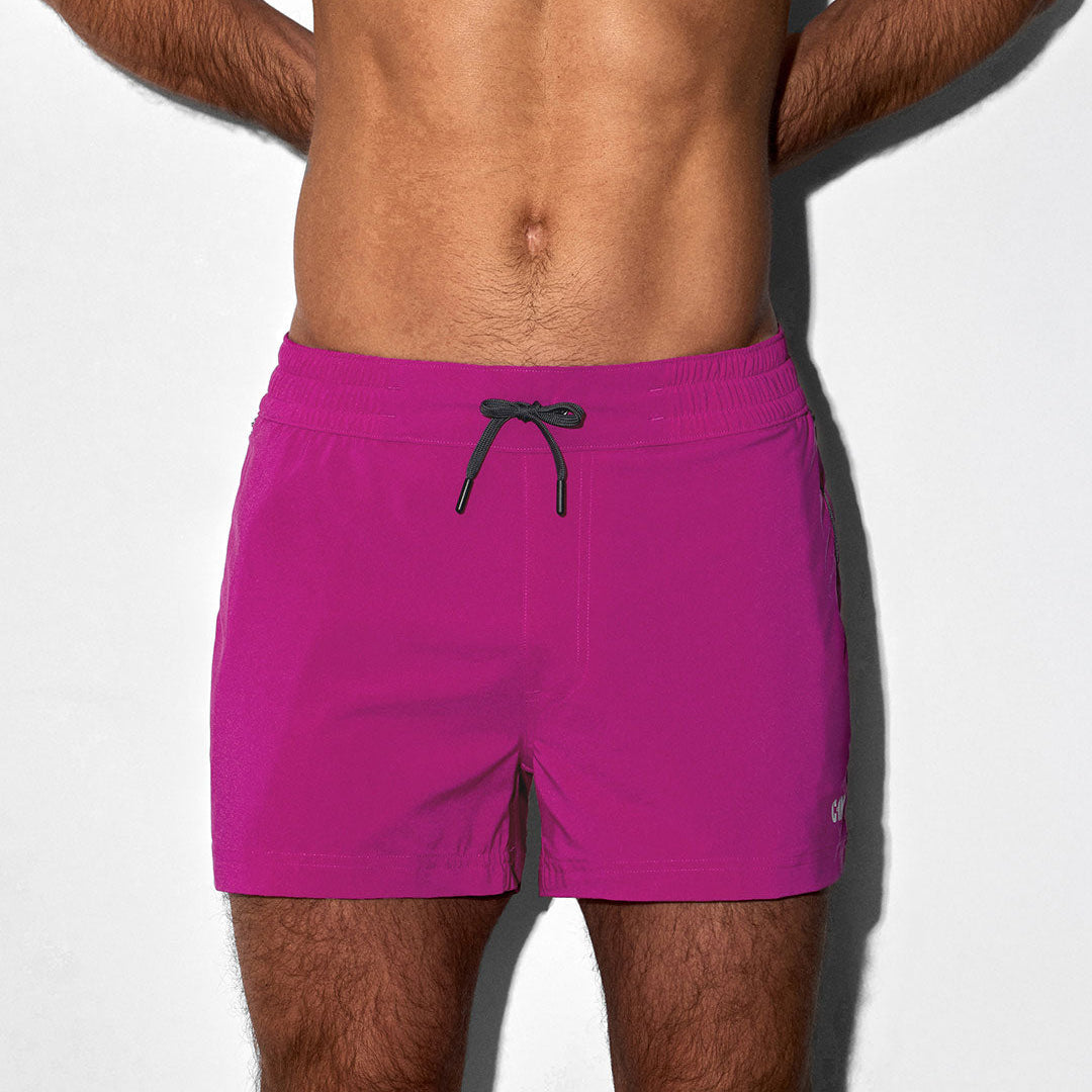 Person wearing bright pink swim shorts on a white background