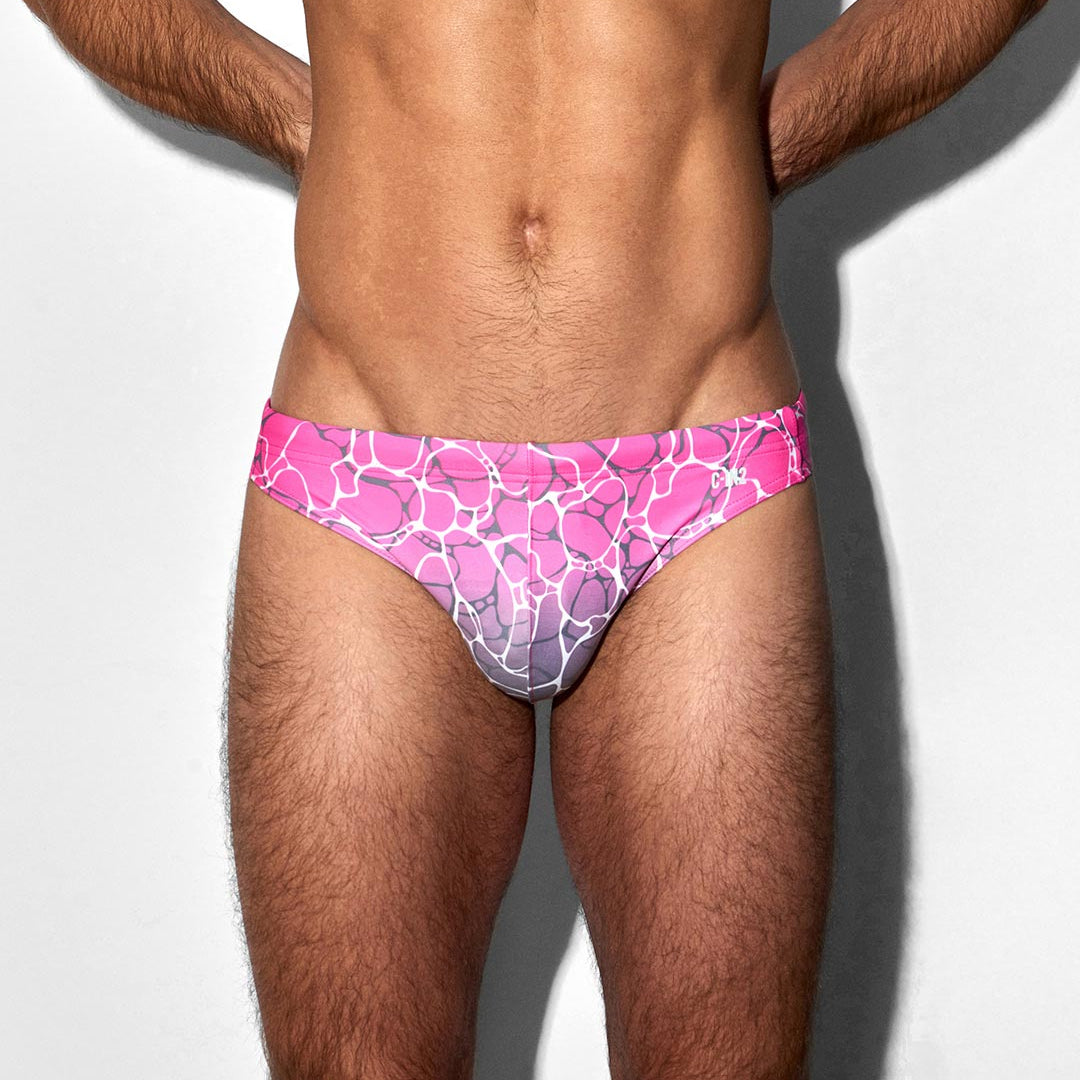Man wearing pink and purple patterned swim briefs on a white background