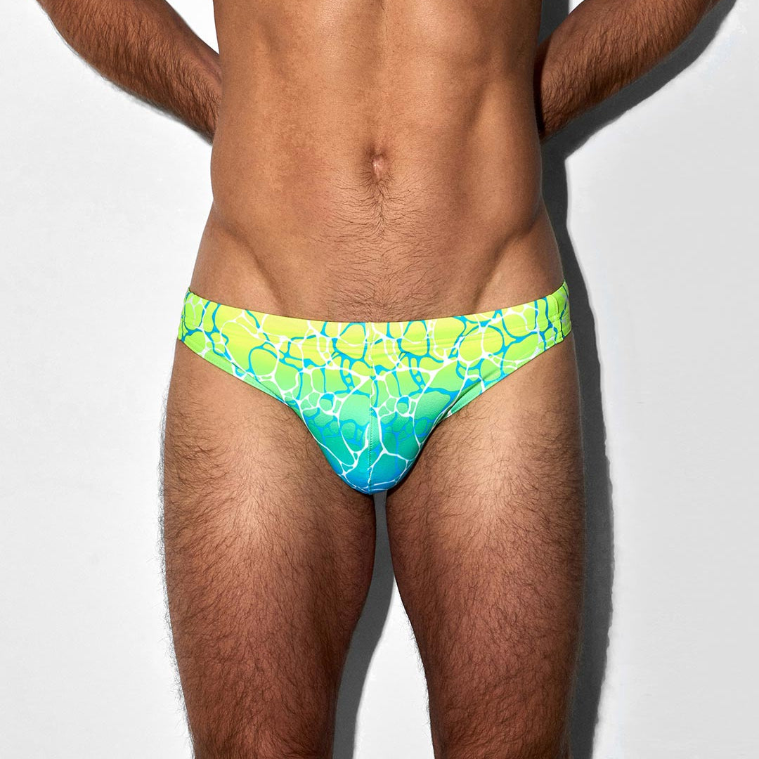 Man wearing a green and blue patterned swim brief on a white background