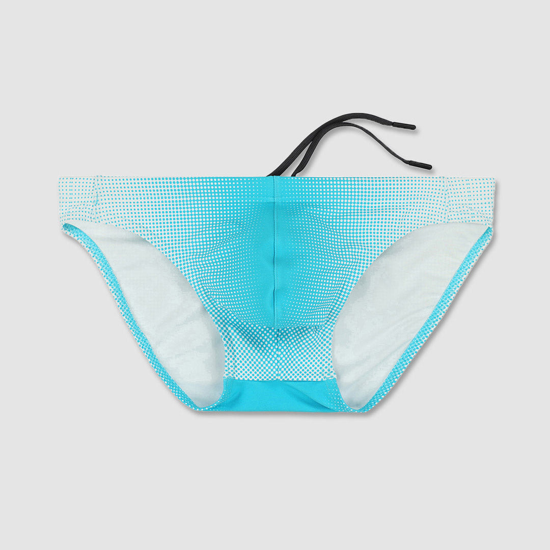 A pair of men's bikini bottoms featuring a turquoise and white micro-dot pattern on the front, a solid turquoise waistband, white lining, and adjustable black side ties, shown against a light gray background.