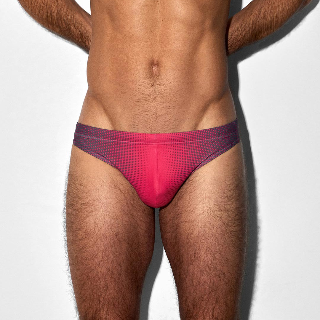 Man wearing a red tanga-style swim brief against a white background