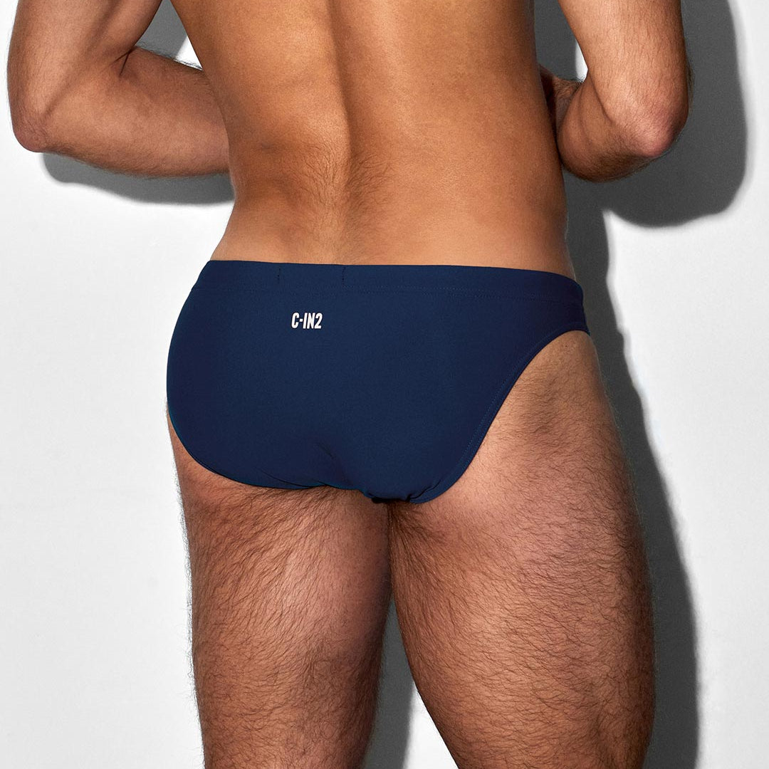 Man wearing a navy blue swim brief tanga with 'C-IN2' branding on a white background