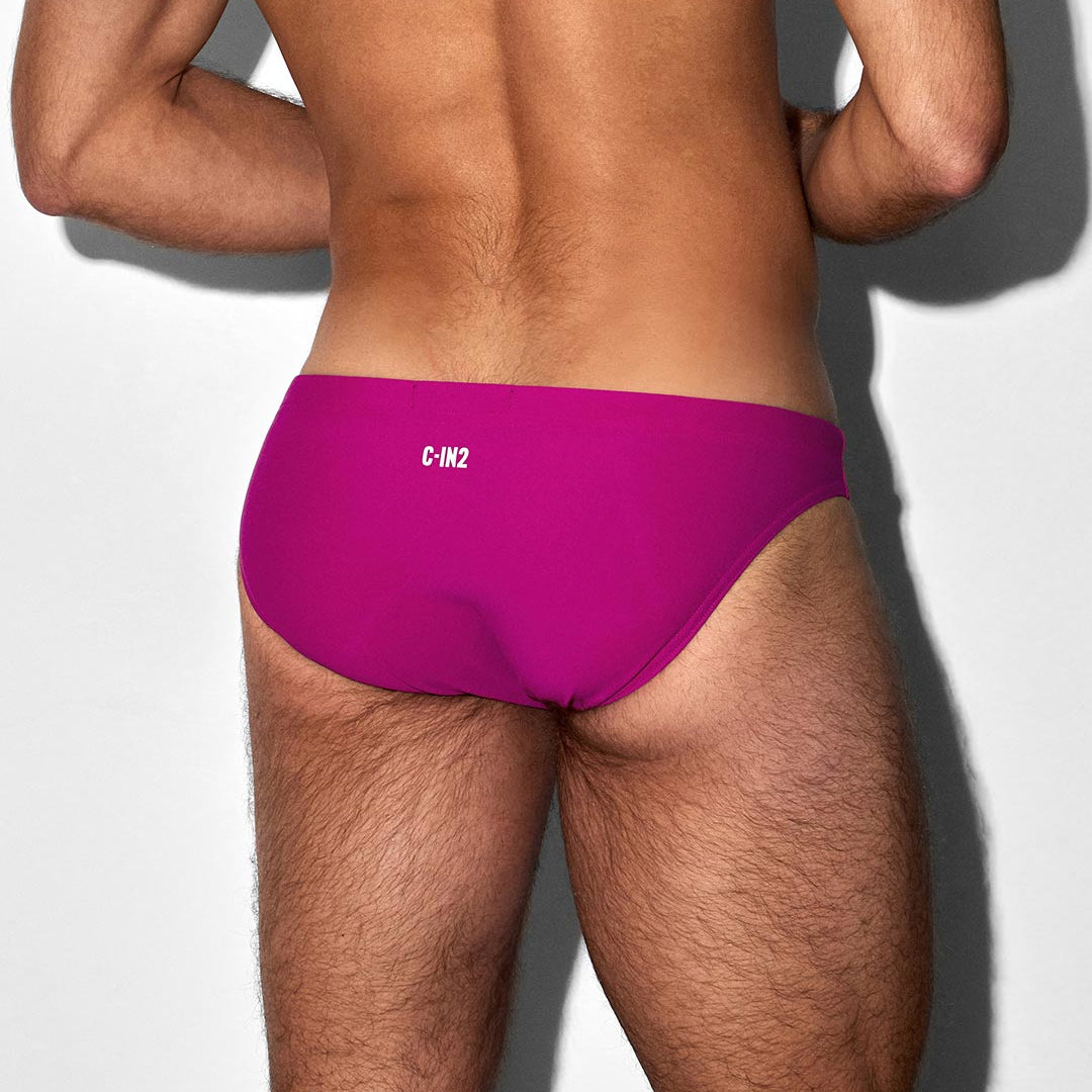 Person wearing bright pink swim briefs with 'C-IN2' branding on a light gray background