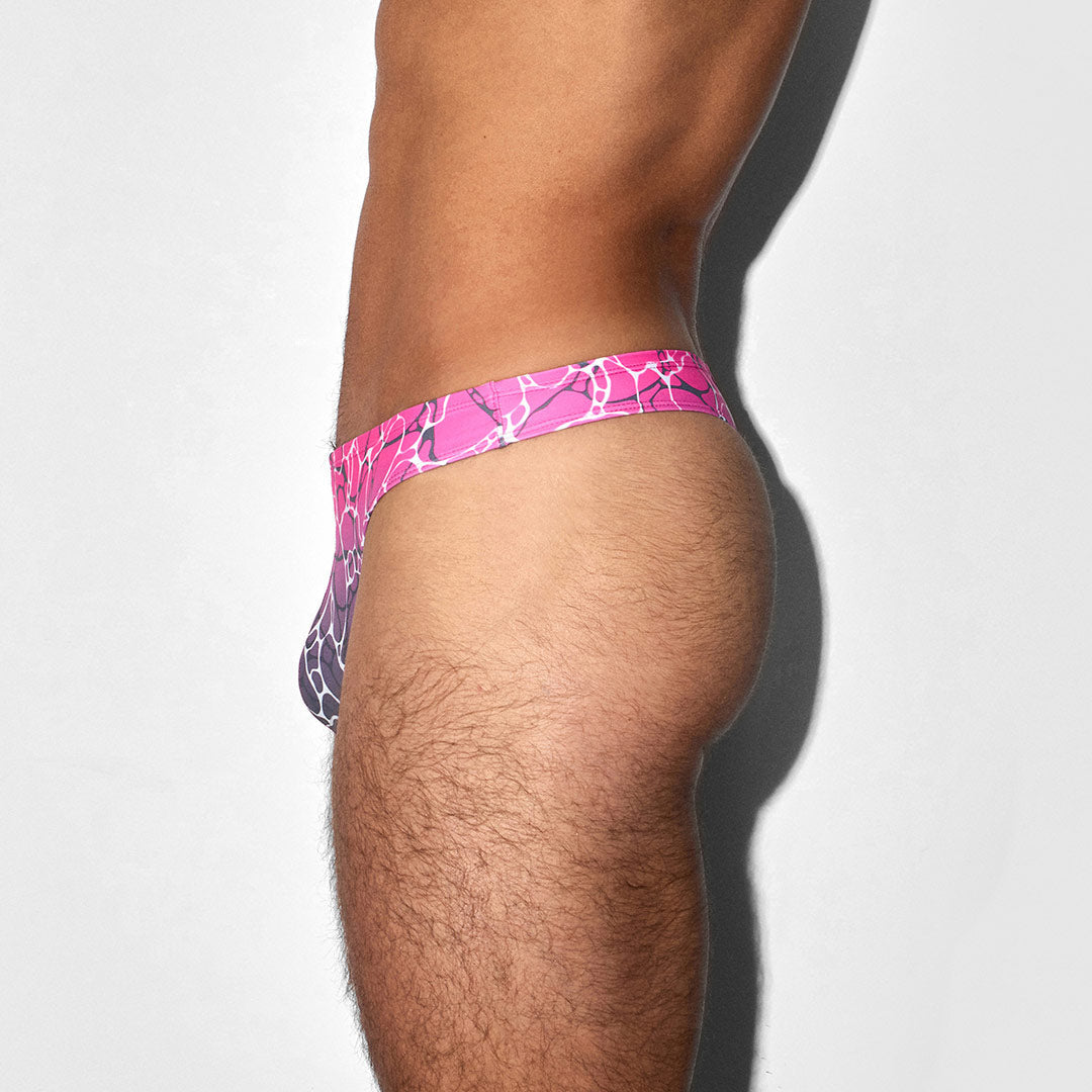 Pink and purple patterned swim thong worn by a person on a white background
