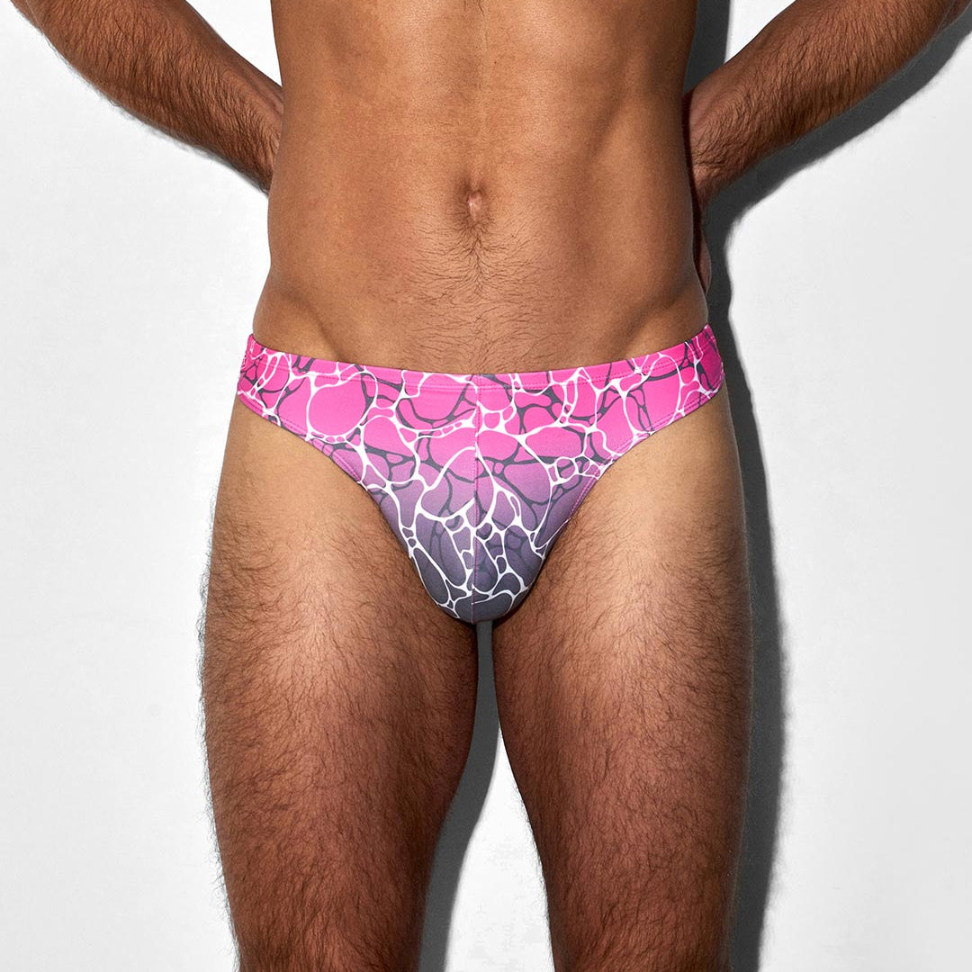Man wearing a pink and purple patterned swim thong on a white background