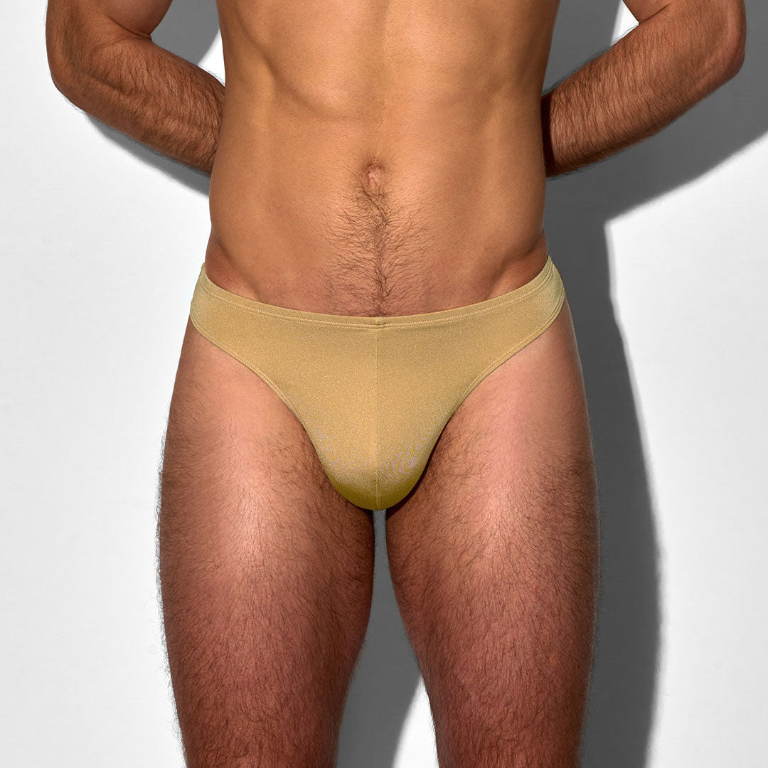 Man wearing a beige men's swim thong on a light gray background