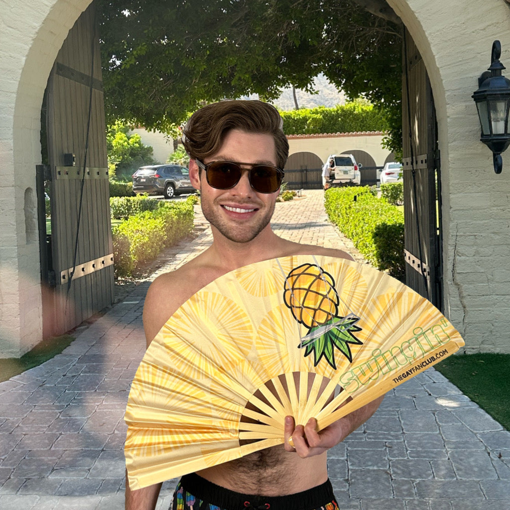 Man holding a pineapple clack fan in front of a driveway with cars and a house in the background.