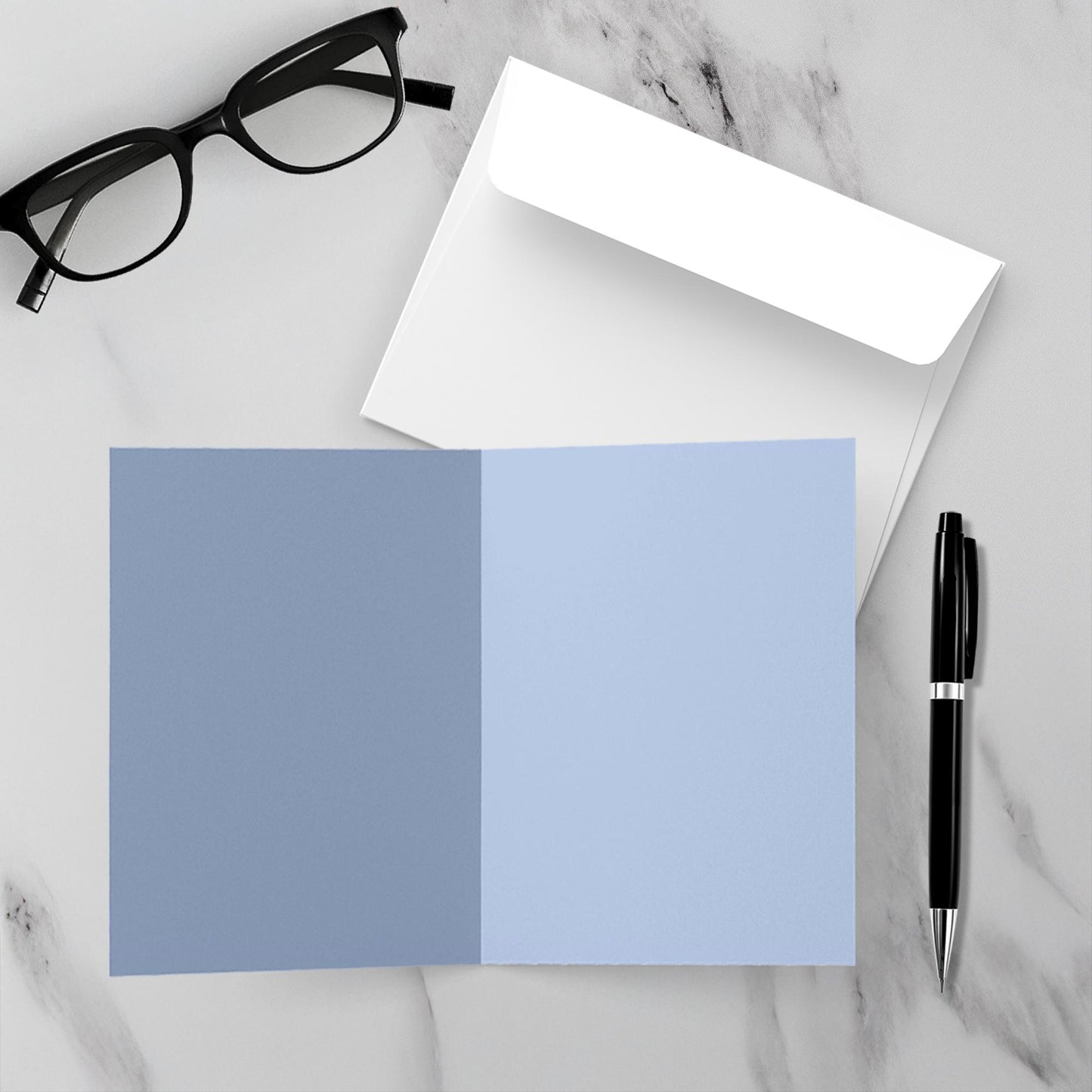 Blank inside card with a blue and white envelope, glasses, and a pen on a marble surface