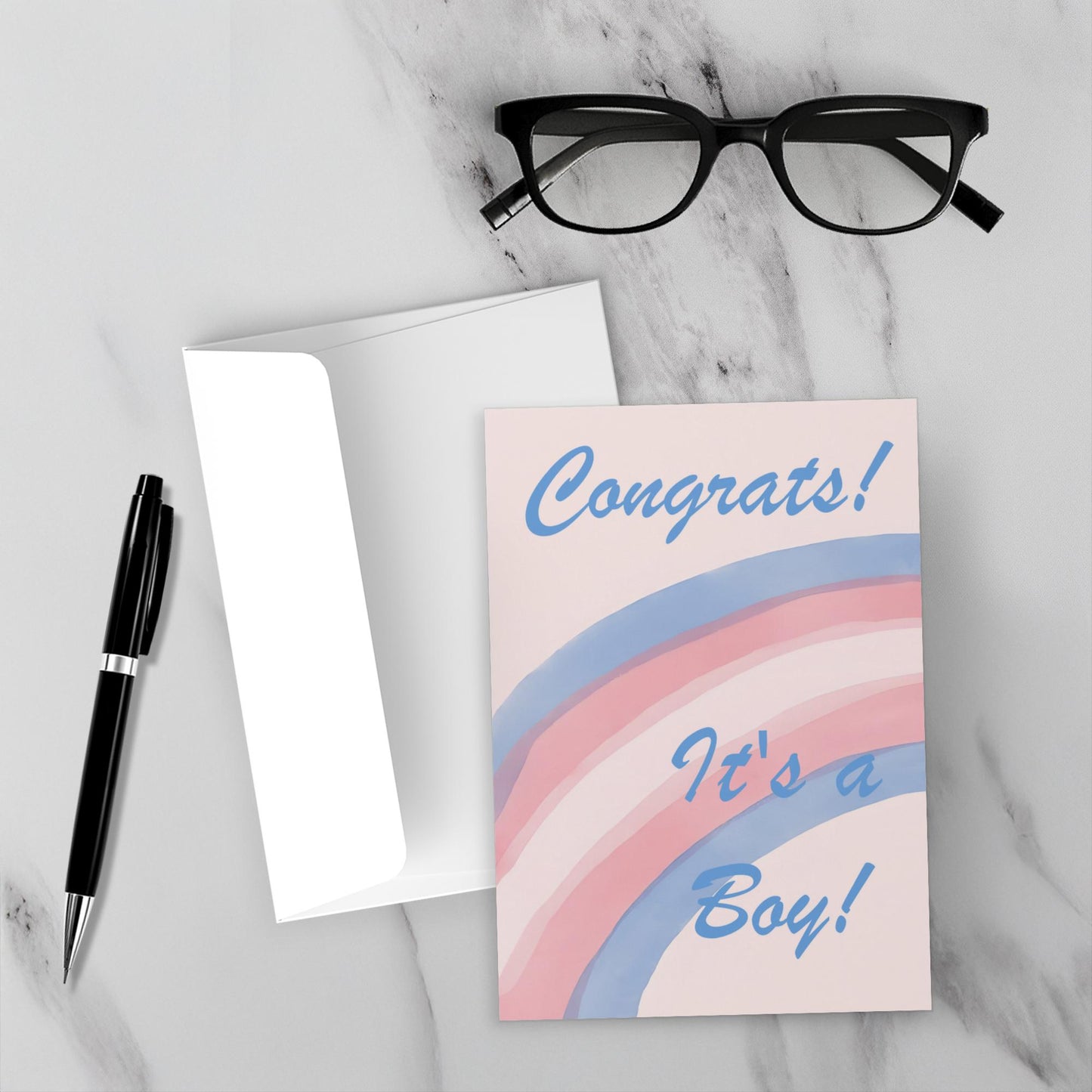 Greeting card with 'Congrats! It's a Boy!' text on a marble surface with glasses and pen.