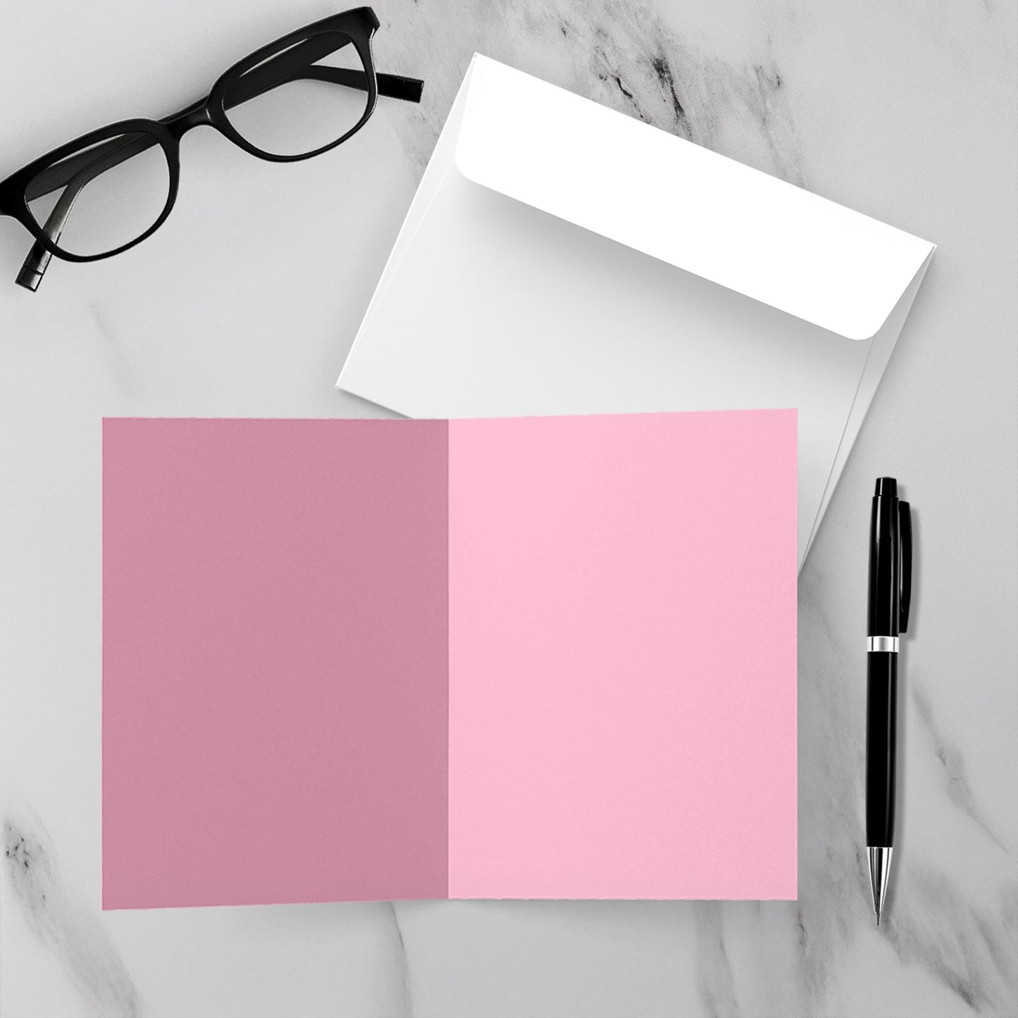 Pink and blank inside card with white envelope, black pen, and glasses on a marble surface