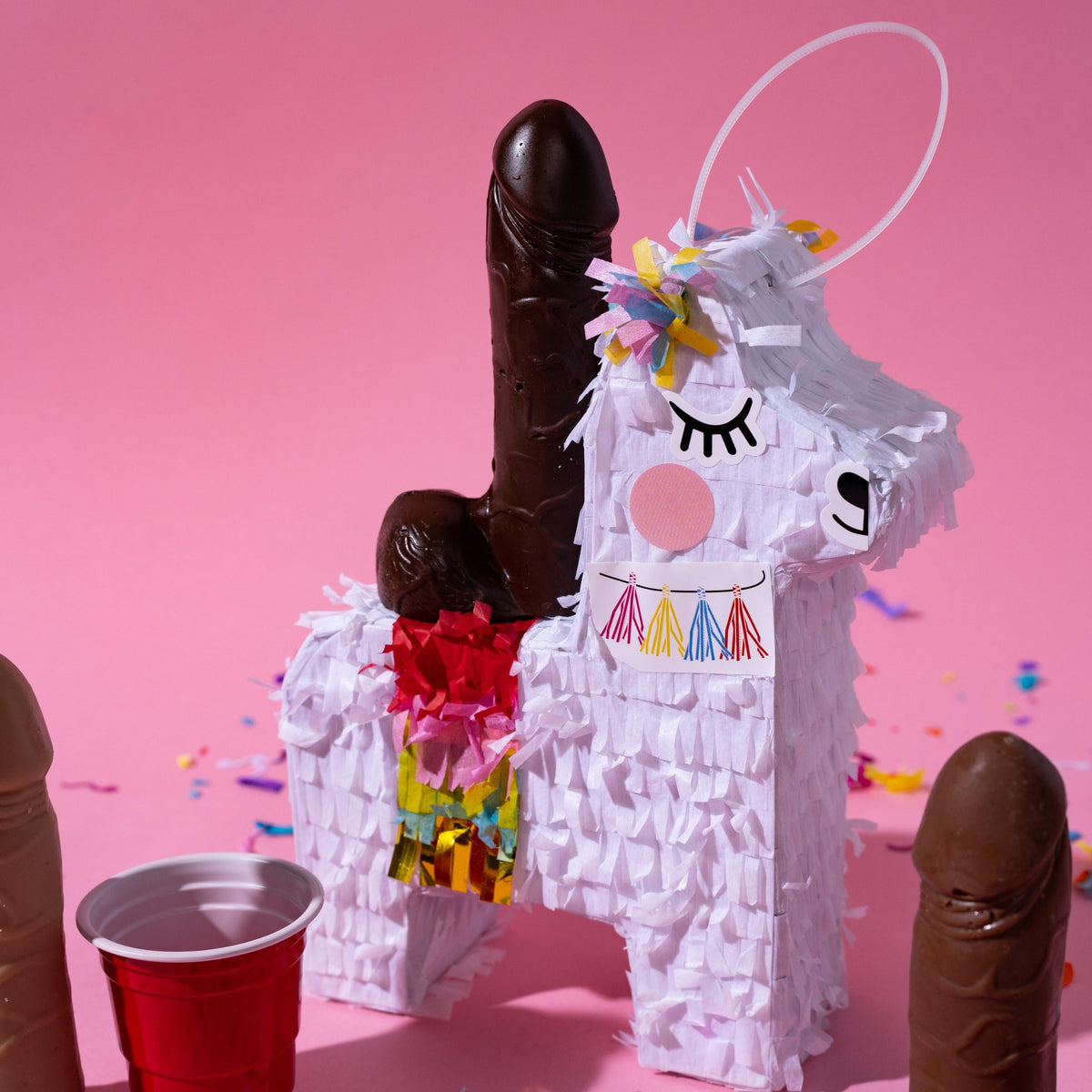 a piñata with a chocolate penis sitting on top against a pink background 