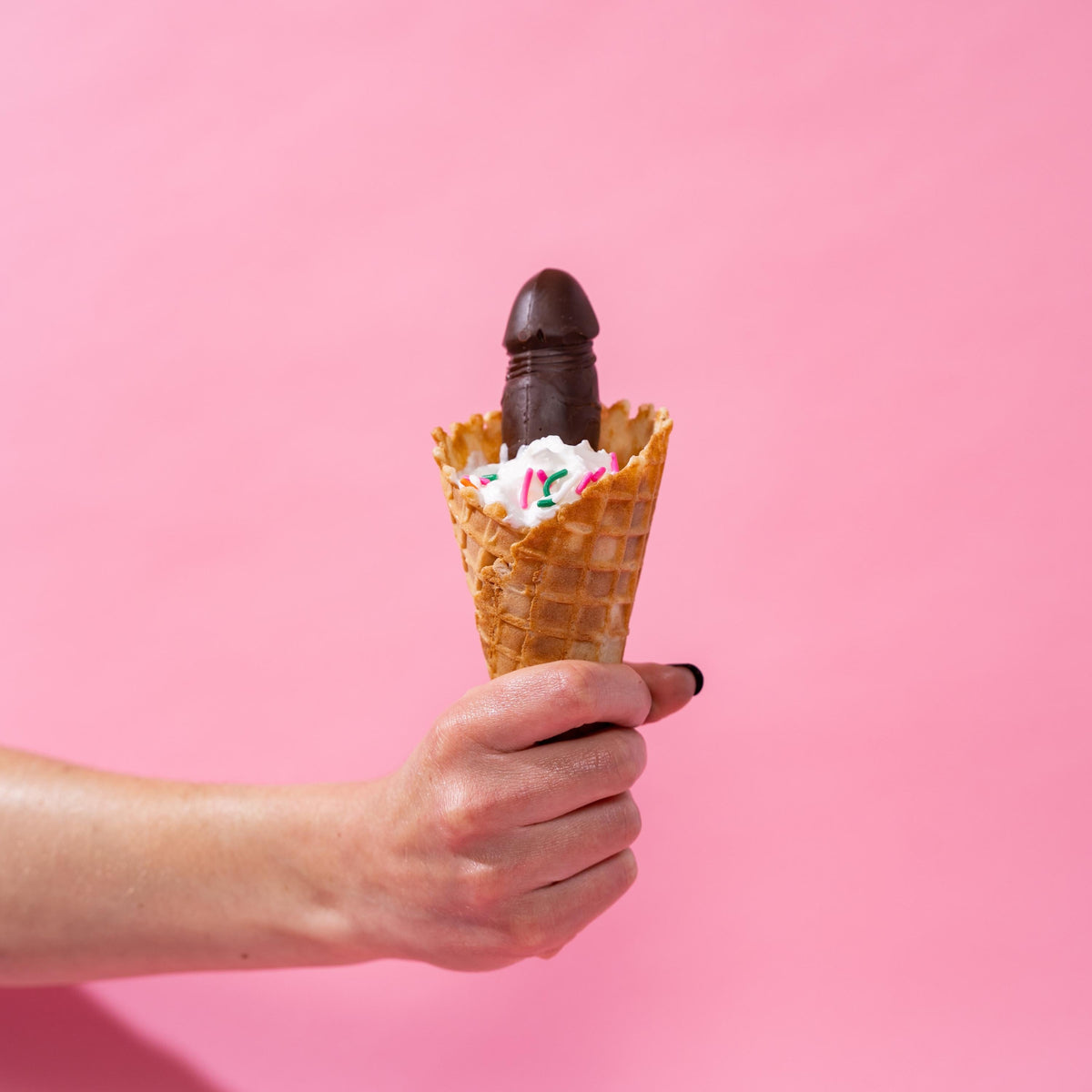 a hand holding out an ice cream cone with a chocolate penis in the ice cream