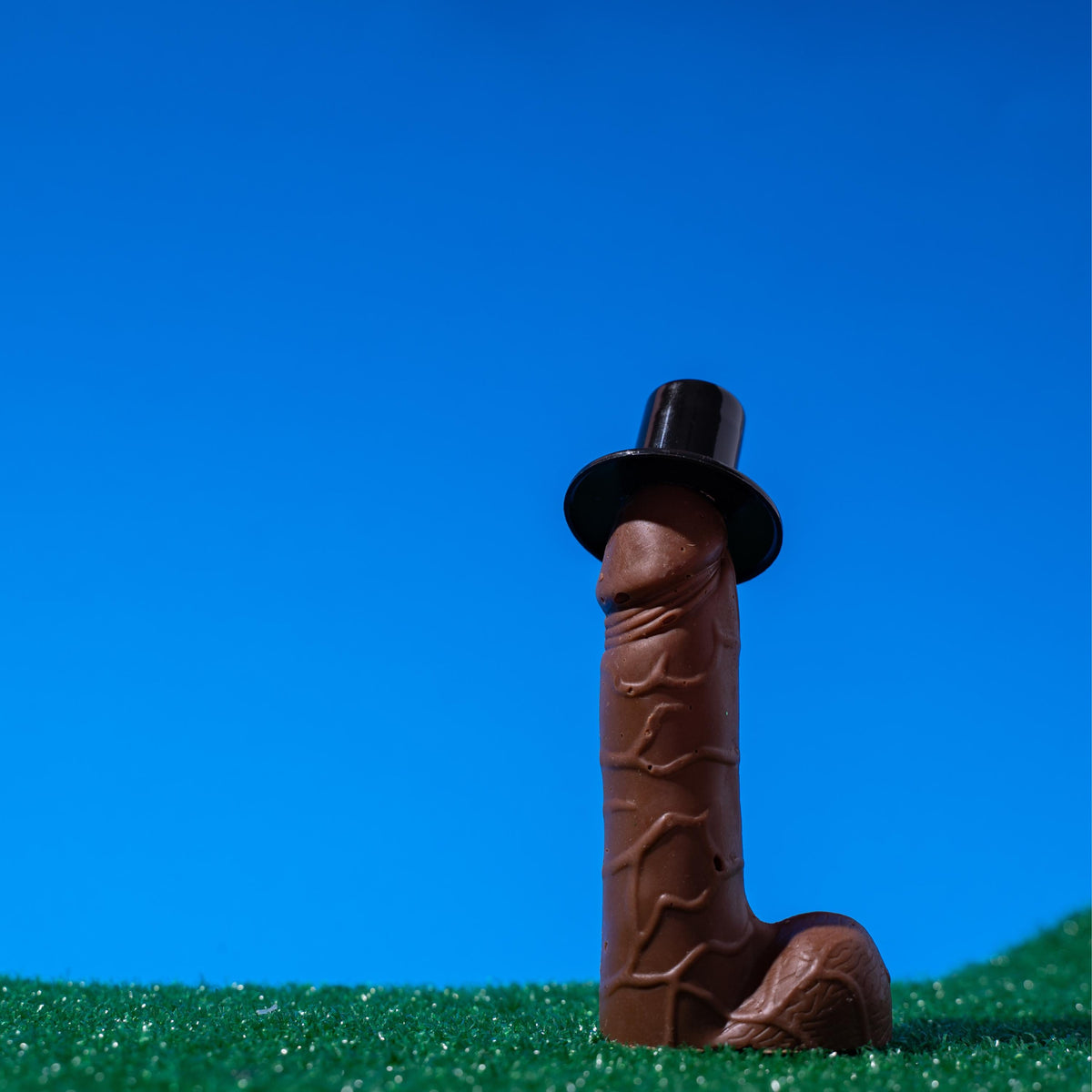 a chocolate penis sitting on green grass against a blue background