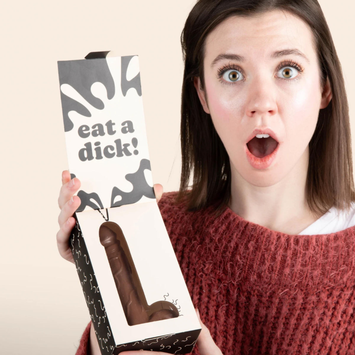 person holding a box with text that reads 'eat a dick!' with a penis shaped chocolate inside