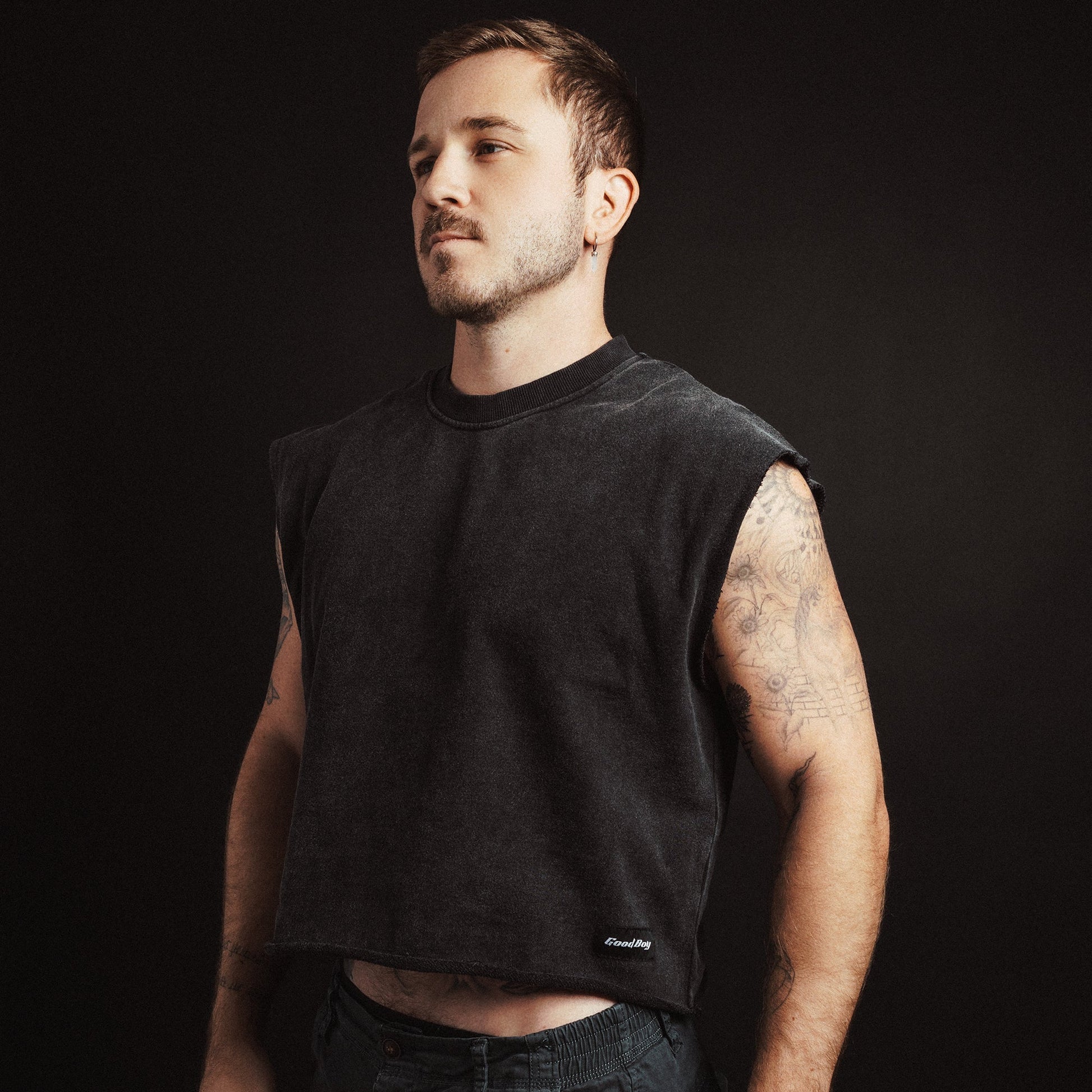 Man wearing a black cropped sleeveless shirt against a dark background